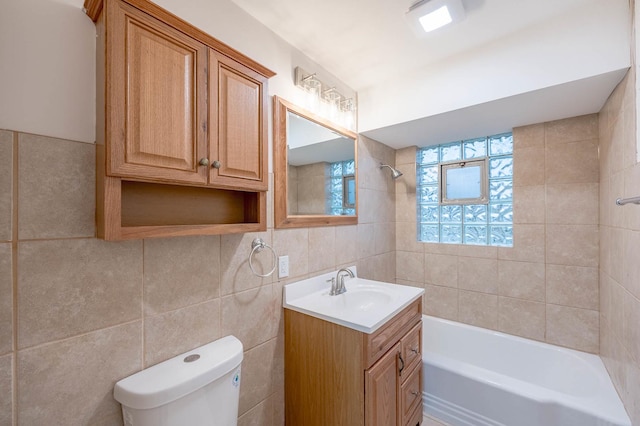 full bathroom featuring tiled shower / bath, vanity, toilet, and tile walls