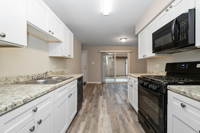 kitchen with hardwood / wood-style floors, black appliances, white cabinets, sink, and light stone countertops