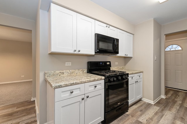 kitchen with black appliances, light stone counters, white cabinetry, and light wood-type flooring