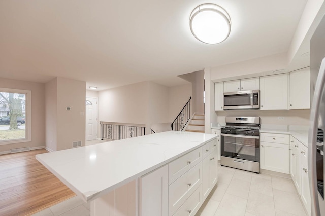 kitchen featuring a center island, light tile patterned flooring, white cabinetry, and appliances with stainless steel finishes