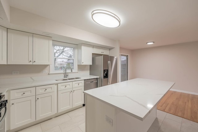 kitchen with a center island, white cabinets, sink, light stone counters, and stainless steel appliances