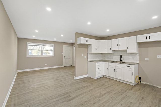 kitchen with light hardwood / wood-style floors, light stone counters, white cabinetry, and sink