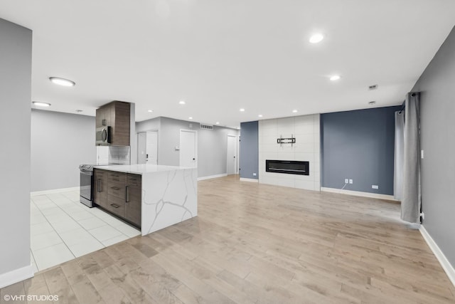 kitchen with light wood-type flooring, a fireplace, appliances with stainless steel finishes, dark brown cabinets, and light stone counters