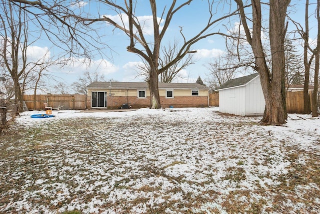 snow covered back of property featuring a storage unit