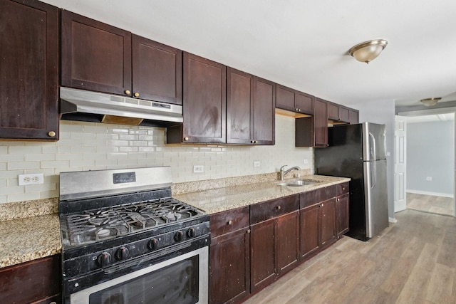 kitchen with backsplash, sink, light stone countertops, light wood-type flooring, and stainless steel appliances