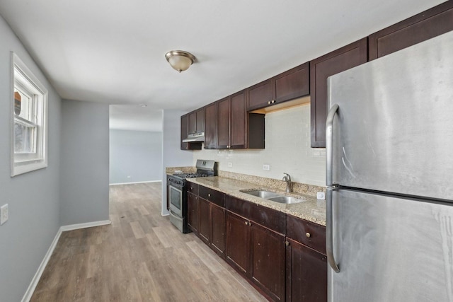 kitchen with light stone countertops, appliances with stainless steel finishes, dark brown cabinets, sink, and light hardwood / wood-style flooring