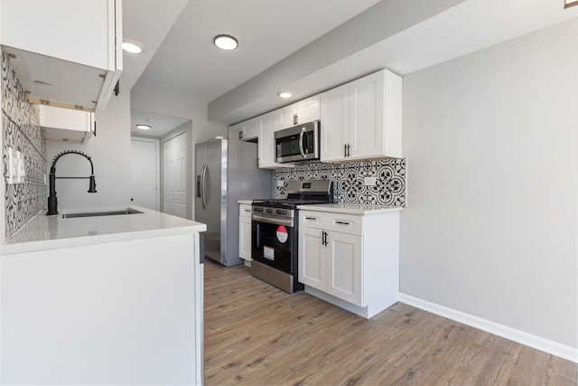 kitchen with light hardwood / wood-style flooring, appliances with stainless steel finishes, sink, white cabinets, and decorative backsplash