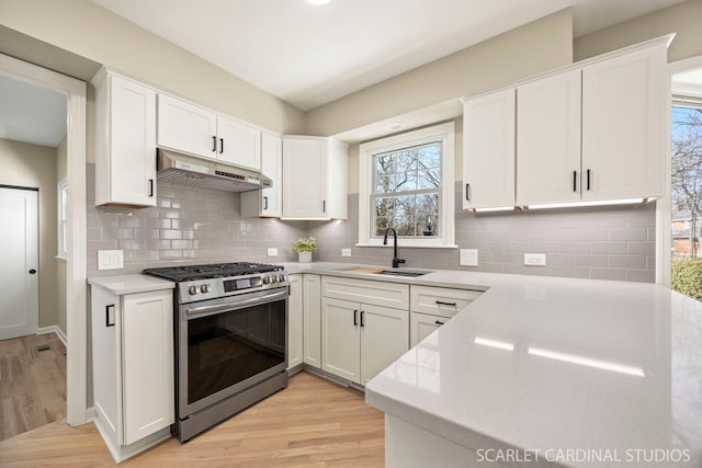 kitchen featuring stainless steel gas range oven, under cabinet range hood, light countertops, white cabinetry, and a sink