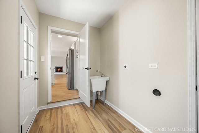 laundry area with light wood-style flooring, a fireplace, baseboards, hookup for an electric dryer, and laundry area