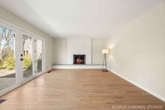 unfurnished living room with visible vents, a brick fireplace, light wood-style floors, and baseboards