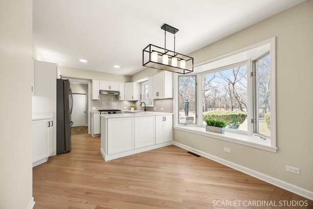 kitchen featuring plenty of natural light, freestanding refrigerator, light countertops, under cabinet range hood, and white cabinetry