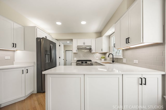 kitchen featuring under cabinet range hood, a sink, stainless steel appliances, white cabinets, and light countertops