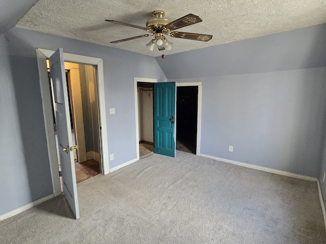 unfurnished bedroom with ceiling fan, carpet floors, a textured ceiling, lofted ceiling, and a walk in closet