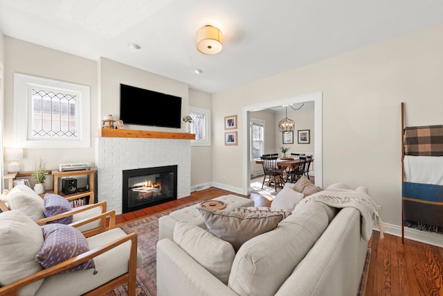 living area with baseboards, a brick fireplace, and wood finished floors