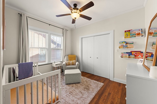 bedroom with a crib, ornamental molding, a closet, baseboards, and dark wood-style flooring