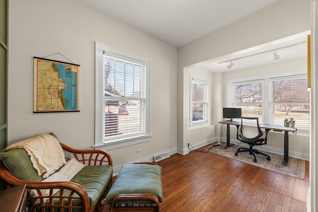 home office featuring plenty of natural light, rail lighting, baseboards, and hardwood / wood-style floors