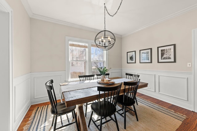 dining room featuring wood finished floors, a decorative wall, wainscoting, crown molding, and a chandelier