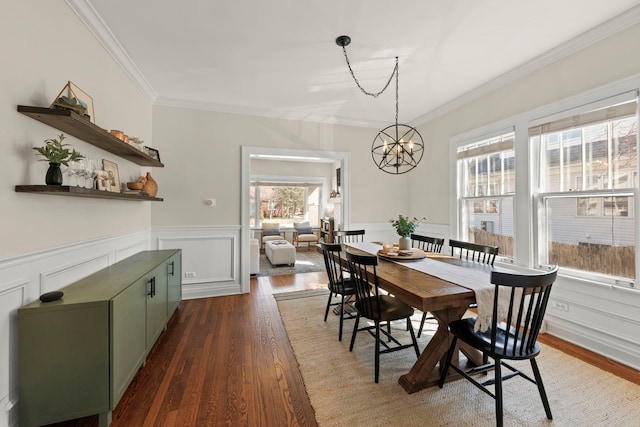 dining area featuring dark wood finished floors, a notable chandelier, wainscoting, and crown molding