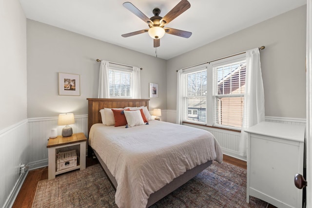 bedroom featuring dark wood-type flooring, a wainscoted wall, and ceiling fan