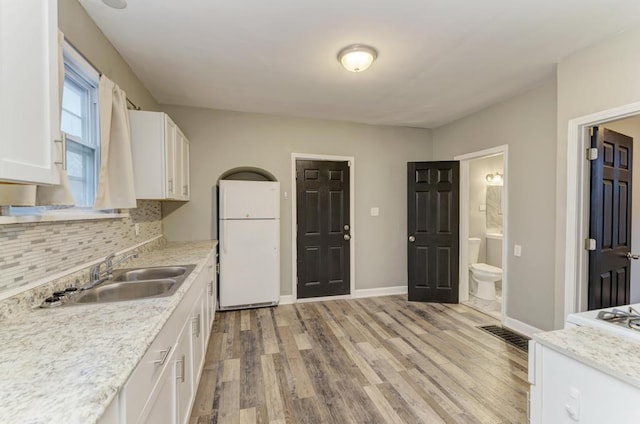 kitchen with tasteful backsplash, light hardwood / wood-style floors, sink, white cabinets, and white fridge