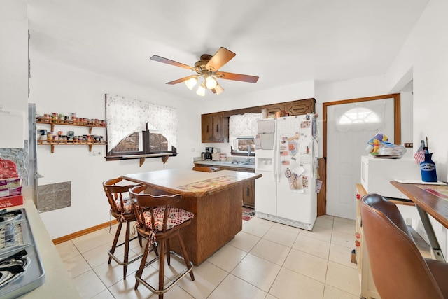 kitchen featuring a kitchen breakfast bar, dark brown cabinets, ceiling fan, white refrigerator with ice dispenser, and a center island