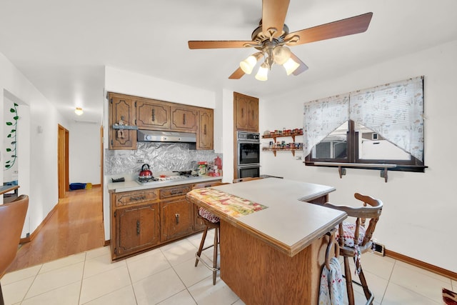 kitchen featuring decorative backsplash, ceiling fan, light tile patterned floors, a center island, and a breakfast bar area