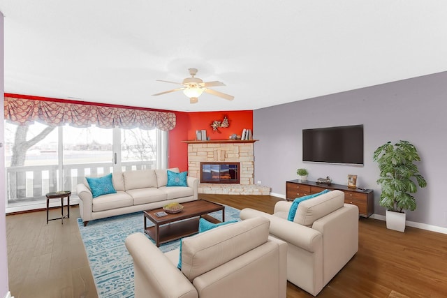 living room featuring hardwood / wood-style floors, ceiling fan, and a stone fireplace