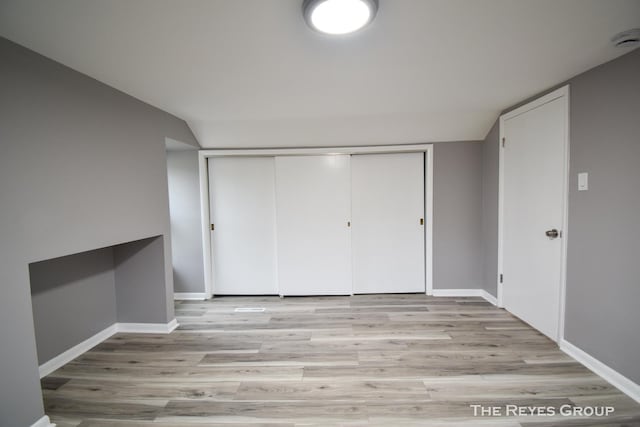 unfurnished bedroom with light hardwood / wood-style floors, vaulted ceiling, and a closet