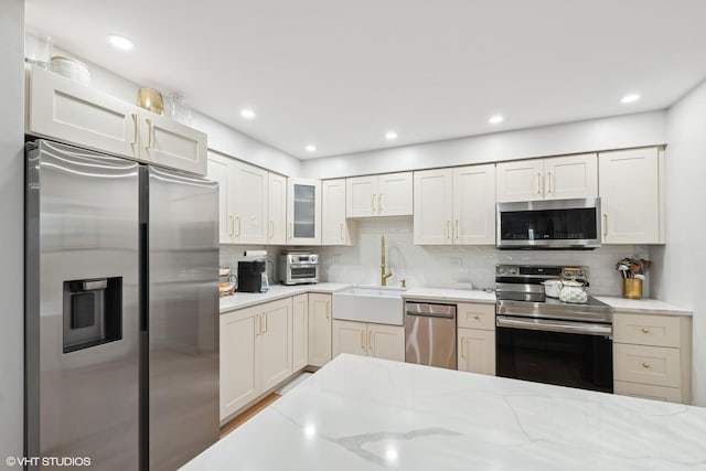 kitchen featuring light stone countertops, white cabinetry, sink, stainless steel appliances, and decorative backsplash