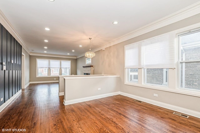 interior space featuring dark wood-type flooring, hanging light fixtures, an inviting chandelier, kitchen peninsula, and crown molding