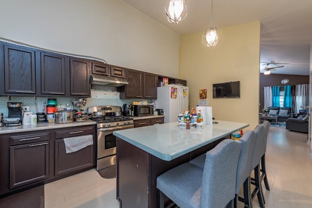 kitchen featuring stainless steel gas range oven, white refrigerator, vaulted ceiling, decorative light fixtures, and a kitchen island