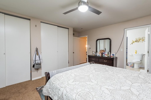 bedroom with ceiling fan, two closets, light colored carpet, and ensuite bath