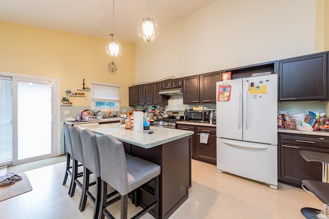 kitchen featuring dark brown cabinetry, pendant lighting, white refrigerator, a center island, and stainless steel range with gas cooktop