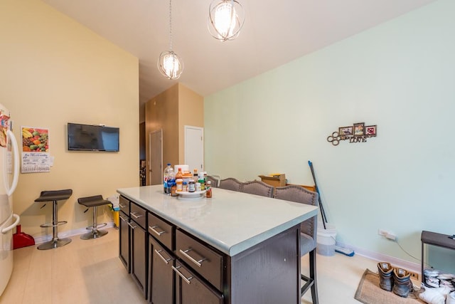 kitchen featuring dark brown cabinetry, white fridge, decorative light fixtures, a kitchen bar, and a kitchen island