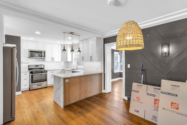 kitchen featuring light hardwood / wood-style floors, stainless steel appliances, white cabinetry, and hanging light fixtures