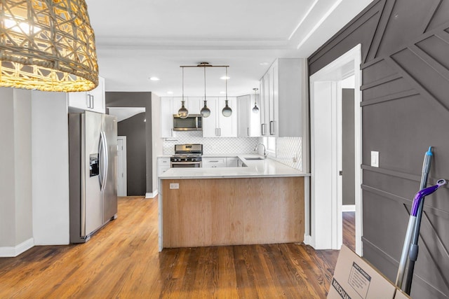 kitchen with kitchen peninsula, hanging light fixtures, stainless steel appliances, white cabinets, and sink