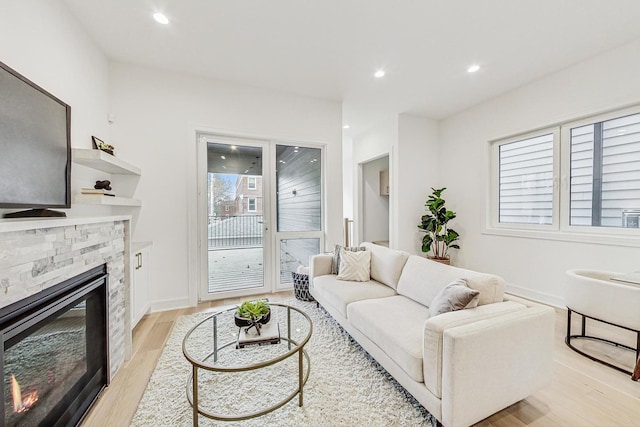 living area featuring light wood-style floors, recessed lighting, a stone fireplace, and baseboards