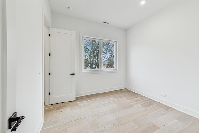 empty room with light wood finished floors, visible vents, and baseboards