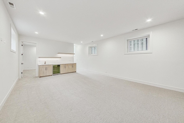 unfurnished living room with wine cooler, recessed lighting, light colored carpet, a sink, and visible vents