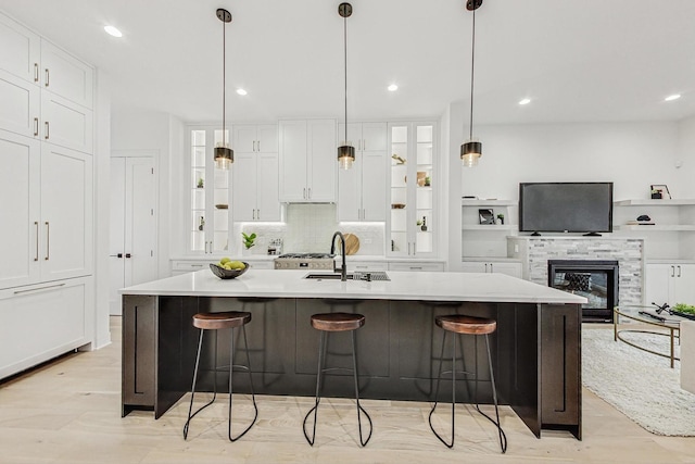 kitchen featuring glass insert cabinets, a large island with sink, light countertops, and a sink