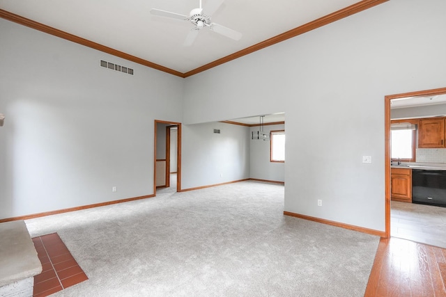 unfurnished living room with sink, crown molding, ceiling fan, a towering ceiling, and light colored carpet