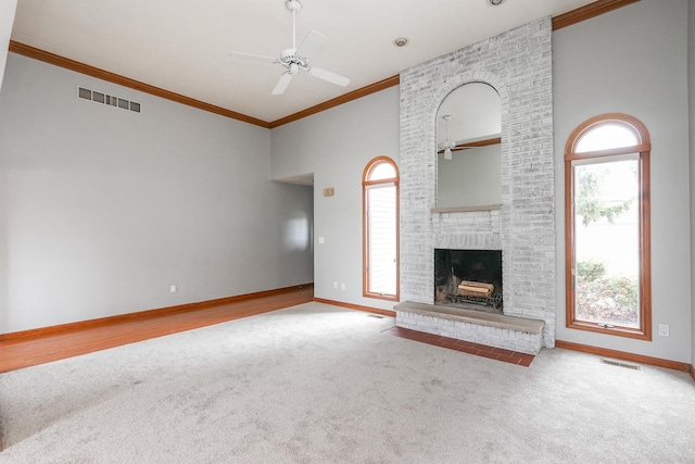 unfurnished living room with ceiling fan, crown molding, light colored carpet, and a brick fireplace