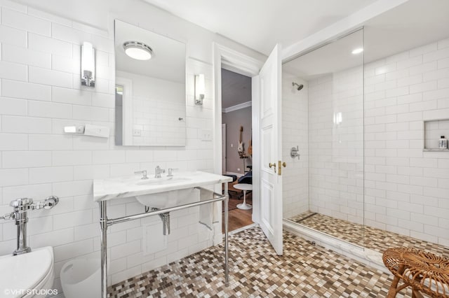 bathroom featuring a tile shower, sink, tile walls, tile patterned flooring, and toilet