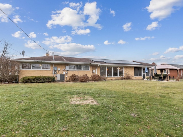 rear view of property with a lawn, solar panels, and central air condition unit