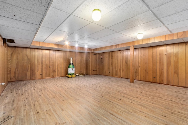 basement featuring a paneled ceiling, wood walls, and light wood-type flooring