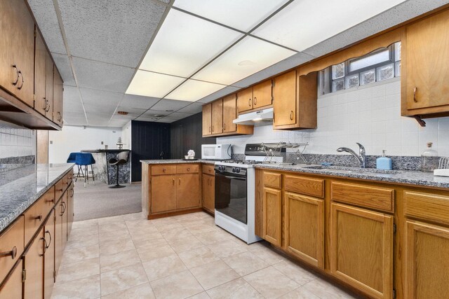 kitchen with a paneled ceiling, white appliances, sink, light stone countertops, and kitchen peninsula