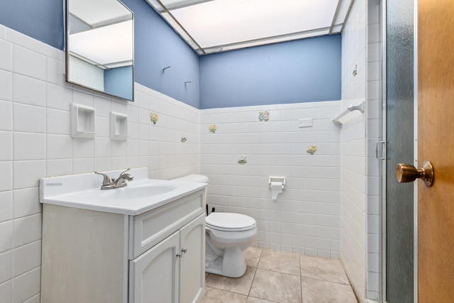 bathroom with tile patterned flooring, toilet, a shower with door, vanity, and tile walls