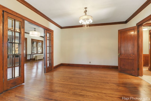 unfurnished room with wood-type flooring, crown molding, an inviting chandelier, radiator, and french doors