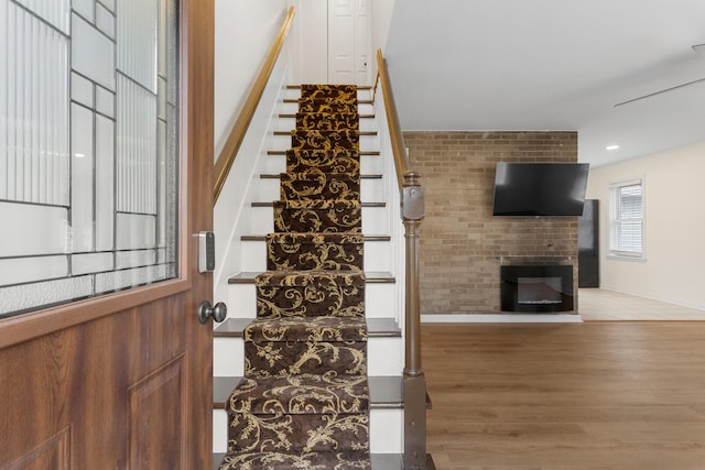 stairway with hardwood / wood-style floors and a brick fireplace