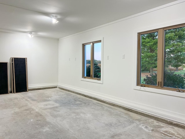 empty room with concrete flooring, plenty of natural light, and crown molding